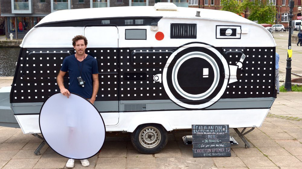 Photographer Brendan Barry stands in front of a giant camera amde out of a caravan