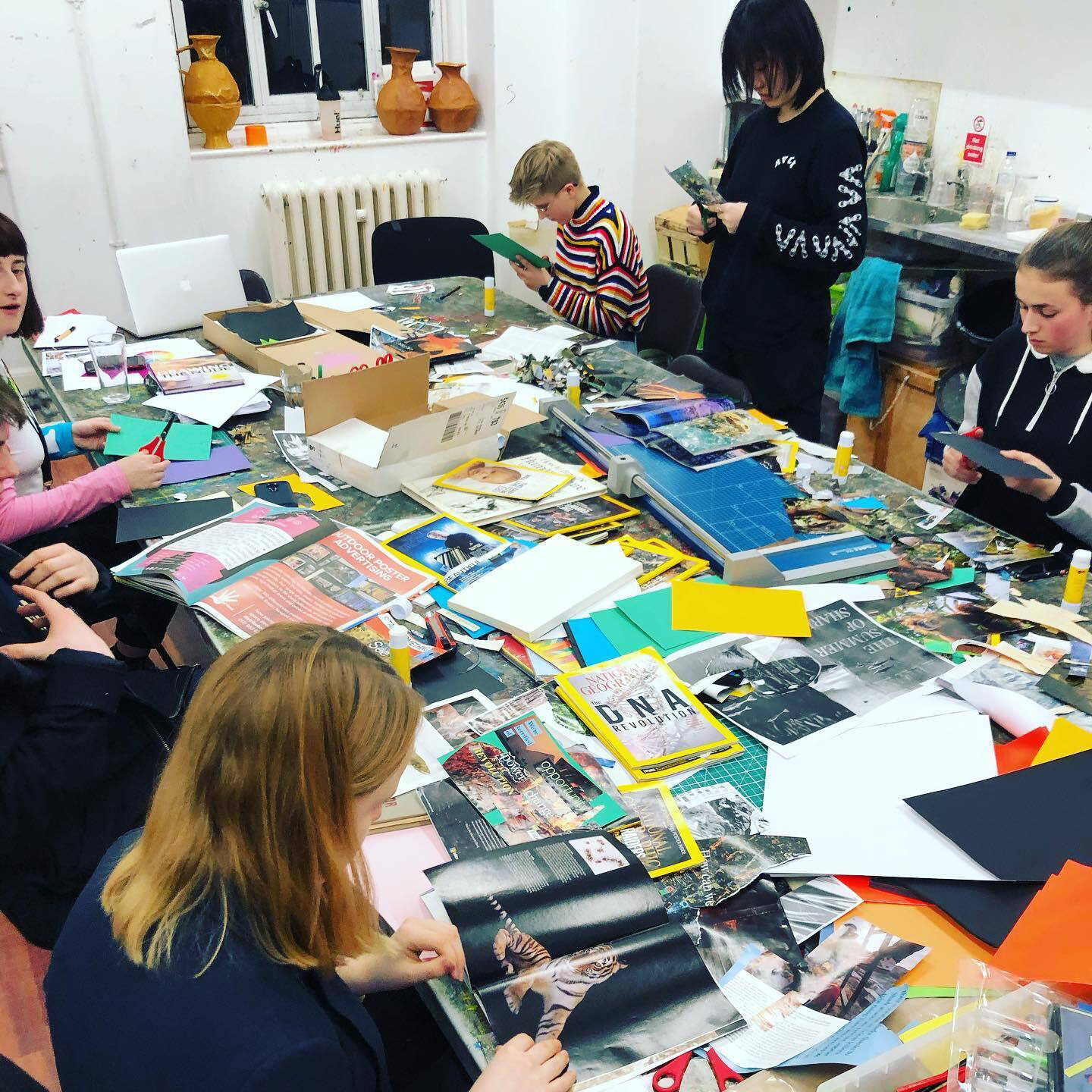 Several young people sitting around a table cutting up magazines and flyers to make a collage