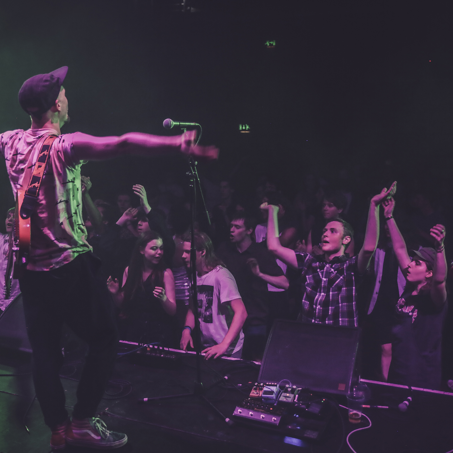 A musician stands on a stage while audience members cheer him on.