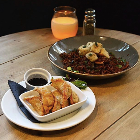 A photograph of vegetable gyoza and a tofu fried rice dish on a wooden table