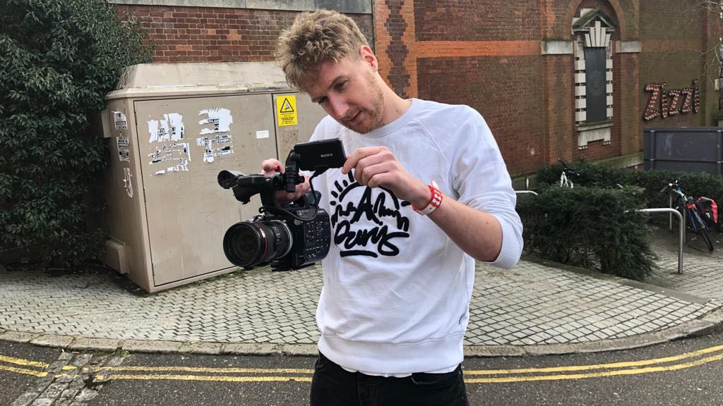 a man stands in front of Exeter Phoenix using a video camera