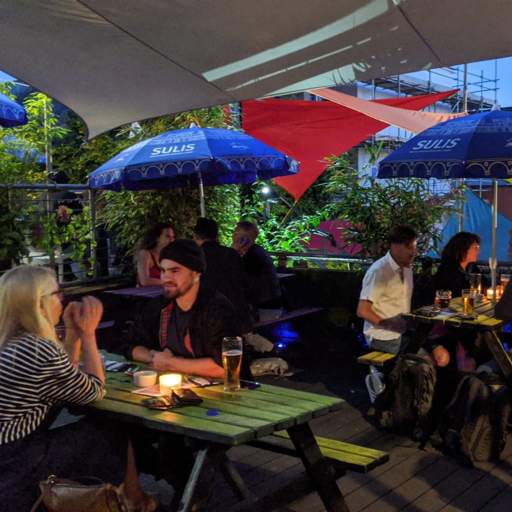 A photo of people sat on colourful picnic benches on the Café Bar terrace