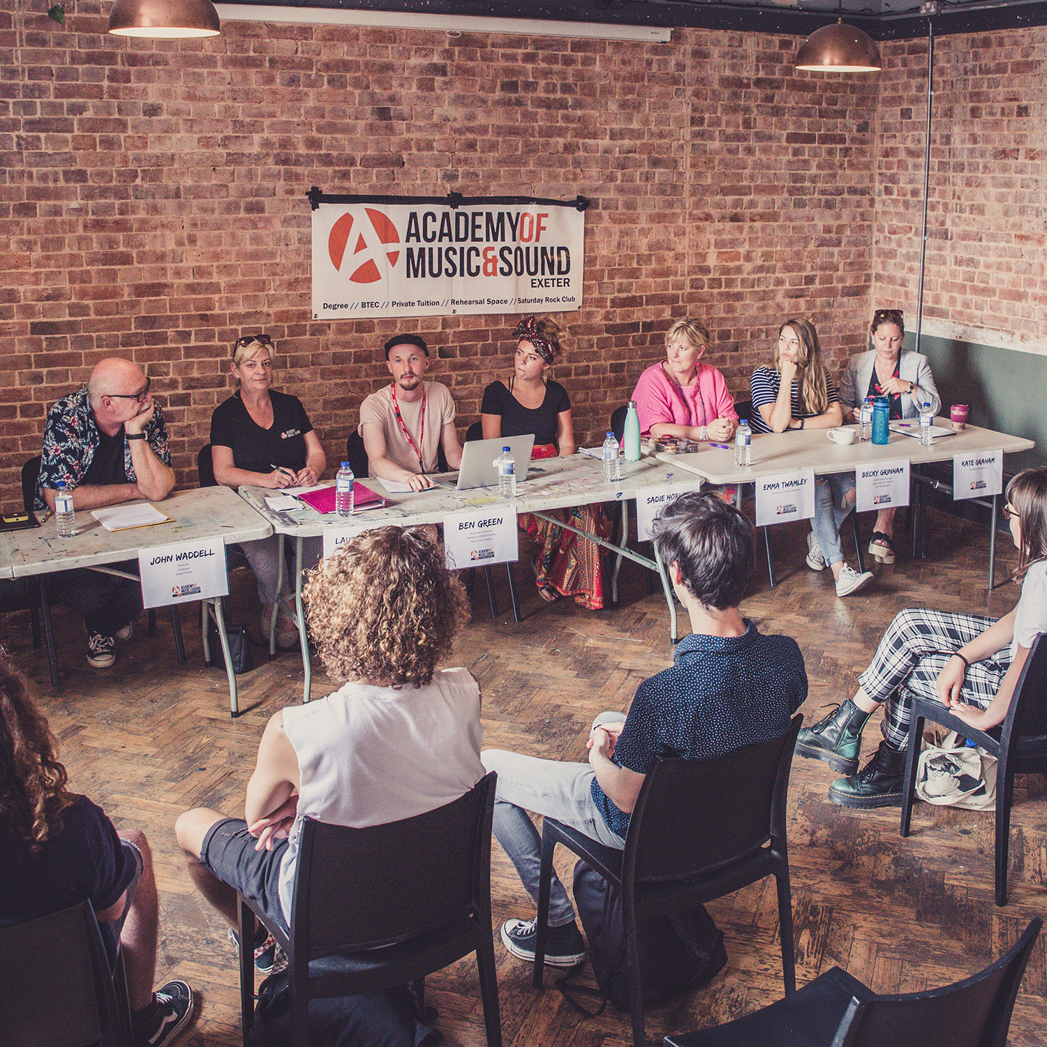 A panel of musicians sit in front of an audience.