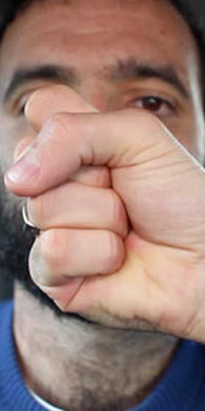 A fist is held in front of a bearded man's face.