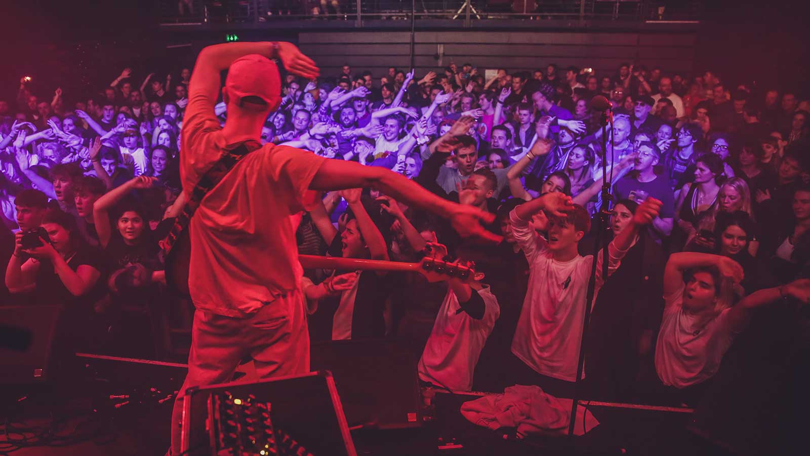 A musician on stage waves his arms while the audience in the background copies him.