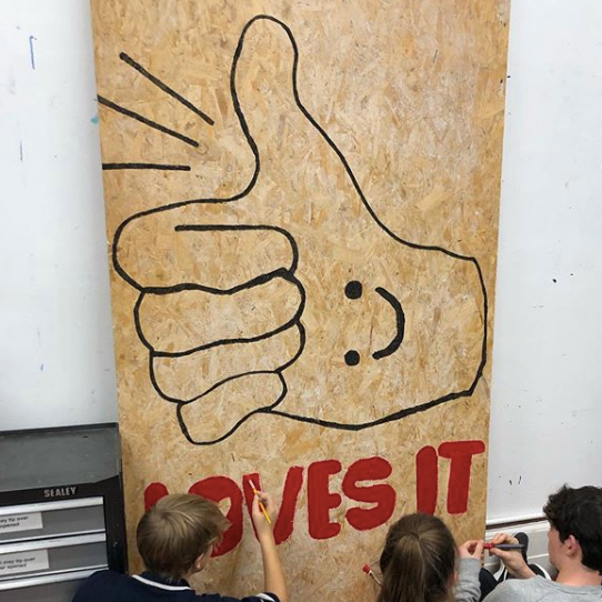 Members of youth group Freefall paint a large scale thumbs up with a smily face in the palm