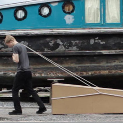 A photograph of a man dragging a large stone with ropes.