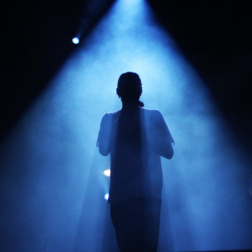 A performer stands on stage backlit with a blue light