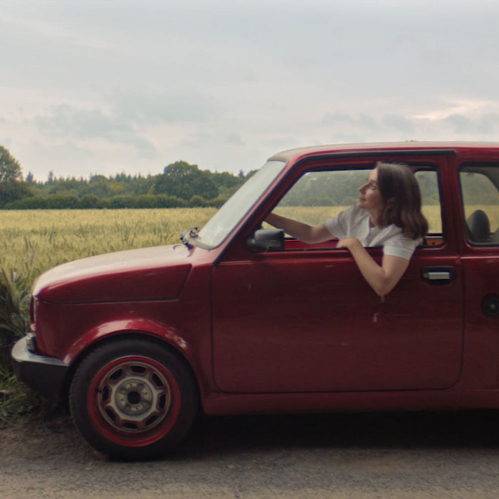 A woman leans out the window of an old fashioned red car