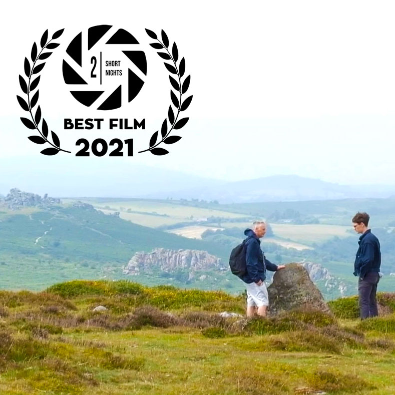 An image of a young man talking to his dad atop a hill in Dartmoor. A laurel at the top left of the image reads 2 Short Nights Best Film 2021