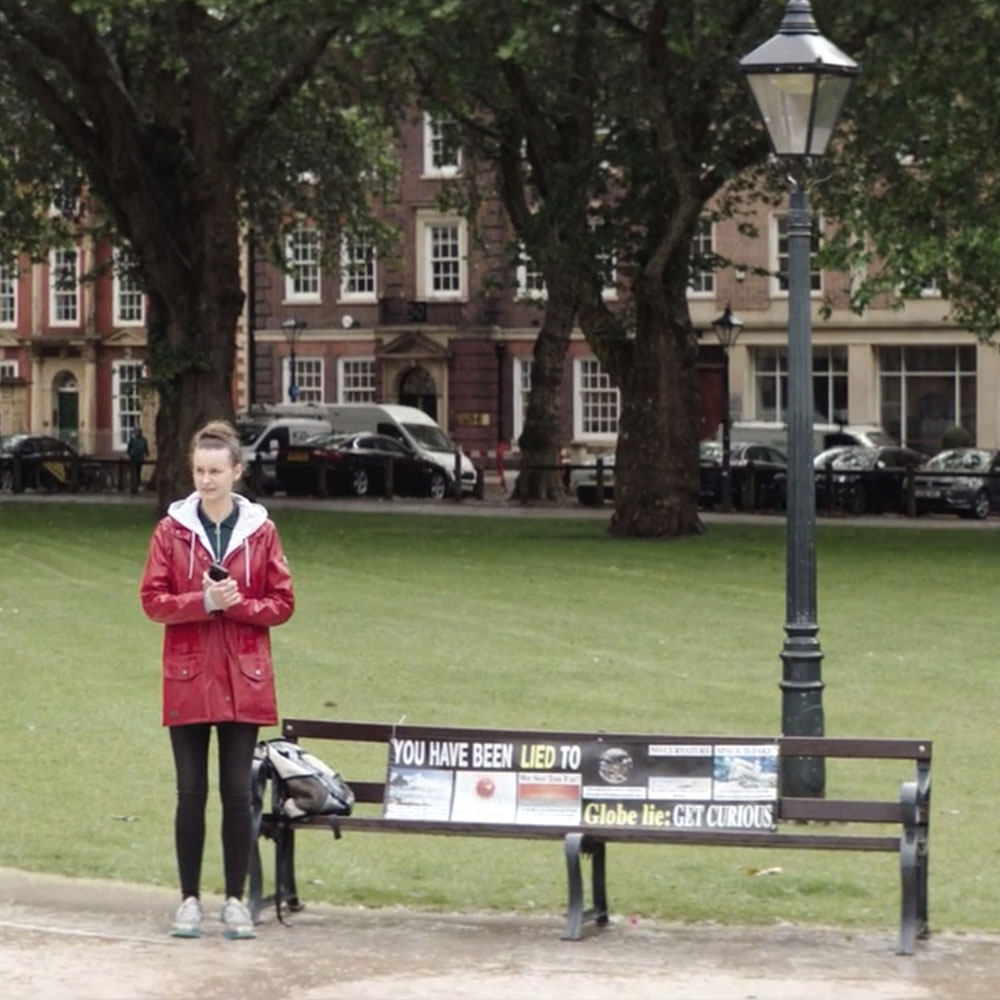 A woman in a red coat stands alone at a bench in a park