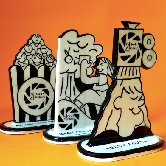 Three ceramic black and white trophies. One shows a bucket of popcorn, one a filmmaker and a tree, and the final is someone under a spotlight