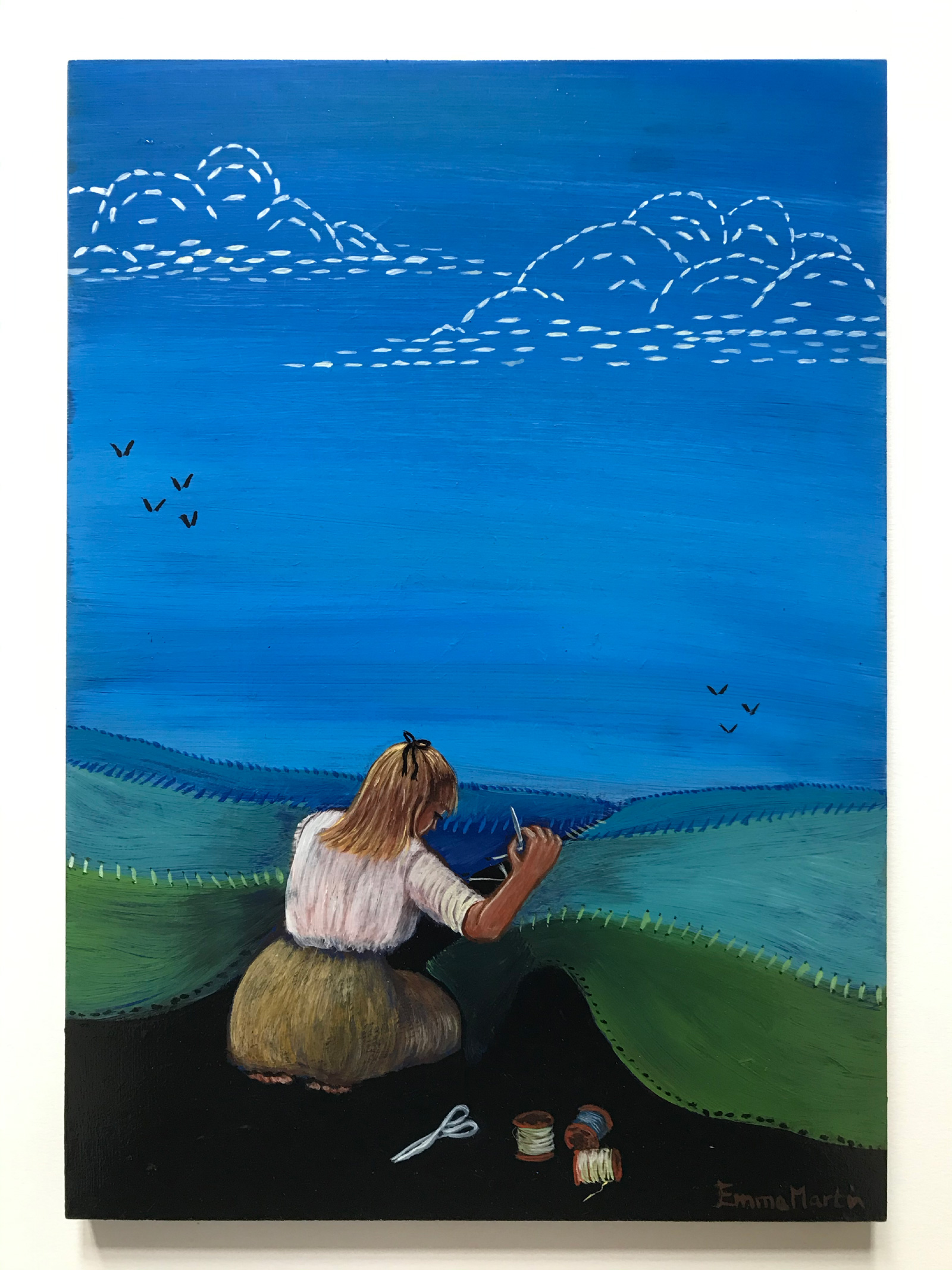 A young woman with blonde hair tied with a black bow, wearing a white blouse and a green skirt, kneels on a black pathway and threads together the green, hilly landscape ahead of her. She has three rolls of thread and a pair of scissors beside her. Above the low green hills, there is a large blue sky with two white threaded clouds. Beneath the left cloud there are four, distant blackbirds and beneath he right cloud and even more distant, there are three.