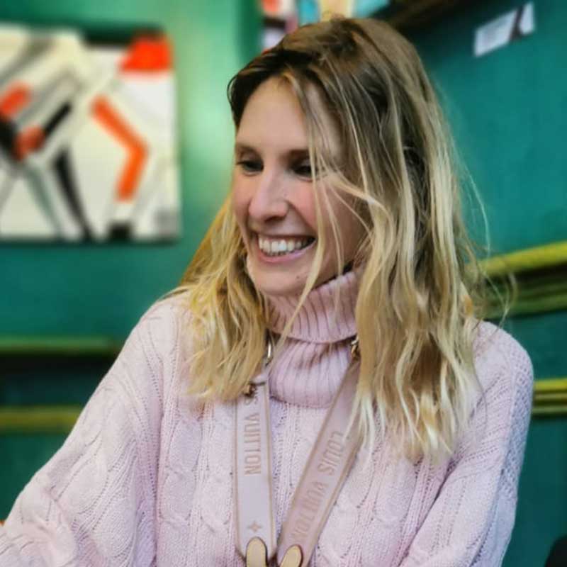 A photograph of artist Isabella Kavanagh sat in a cafe wearing a fuzzy pink jumper.