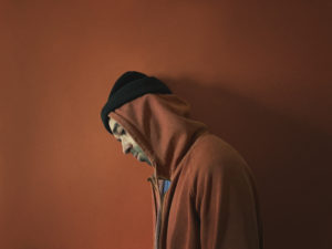 Artist Laundromat stands against a brown wall in the same coloured hoody with his head down
