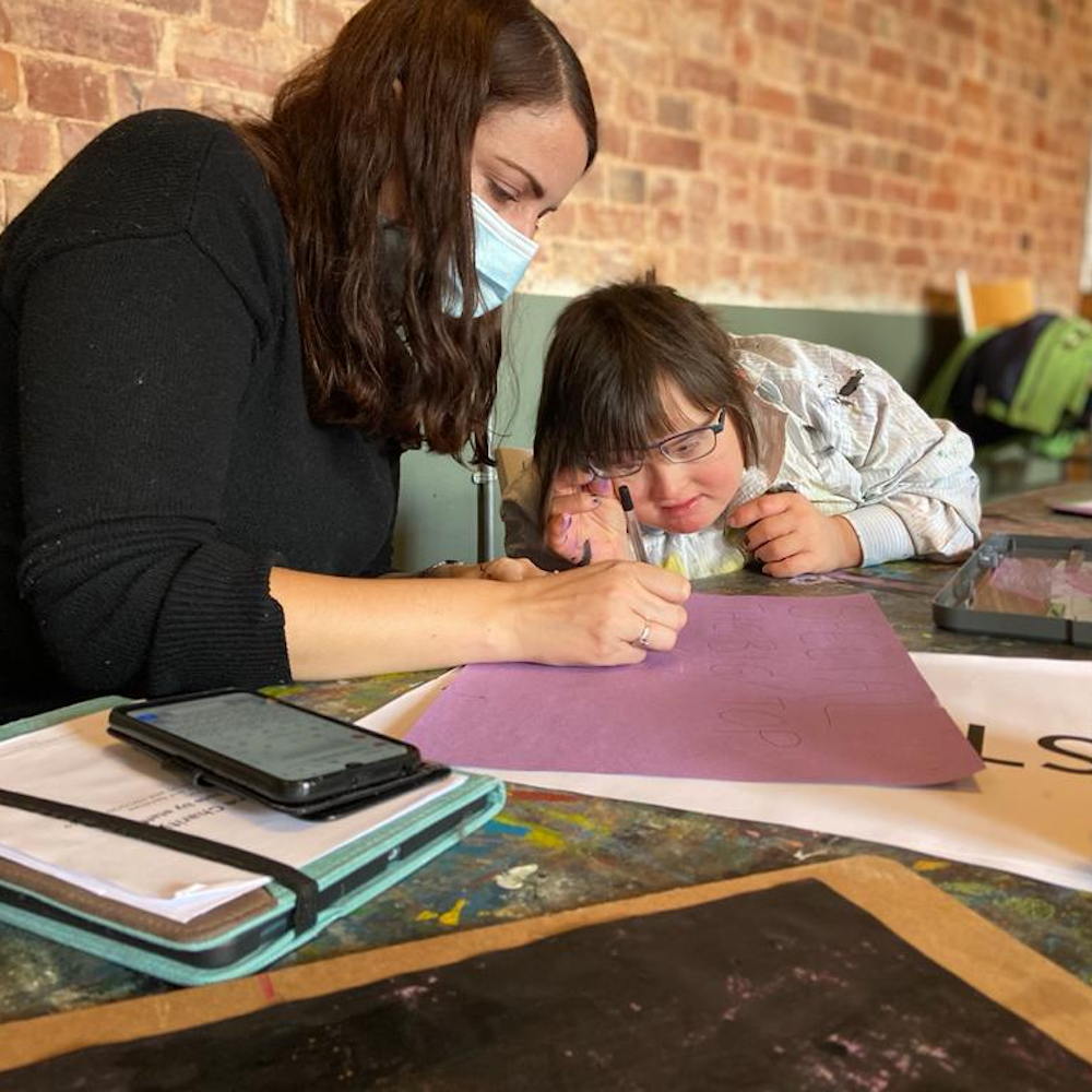 A woman is sat with a young girl drawing as part of the freefall+ project