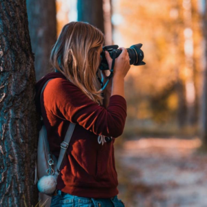 A woman taking a picture with a digital camera in the woods