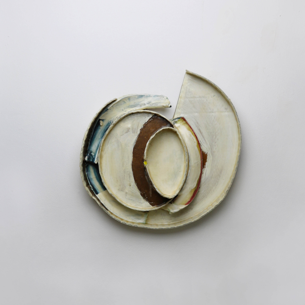 A wall sculpture comprised of abstract circular forms, painted mostly white with stokes of blues and browns.