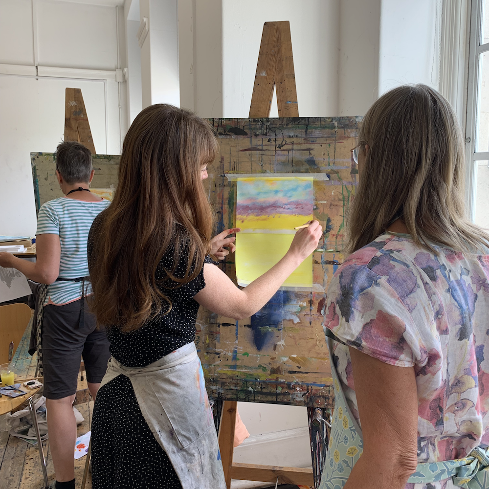 Two women looking at a yellow painting on an easel