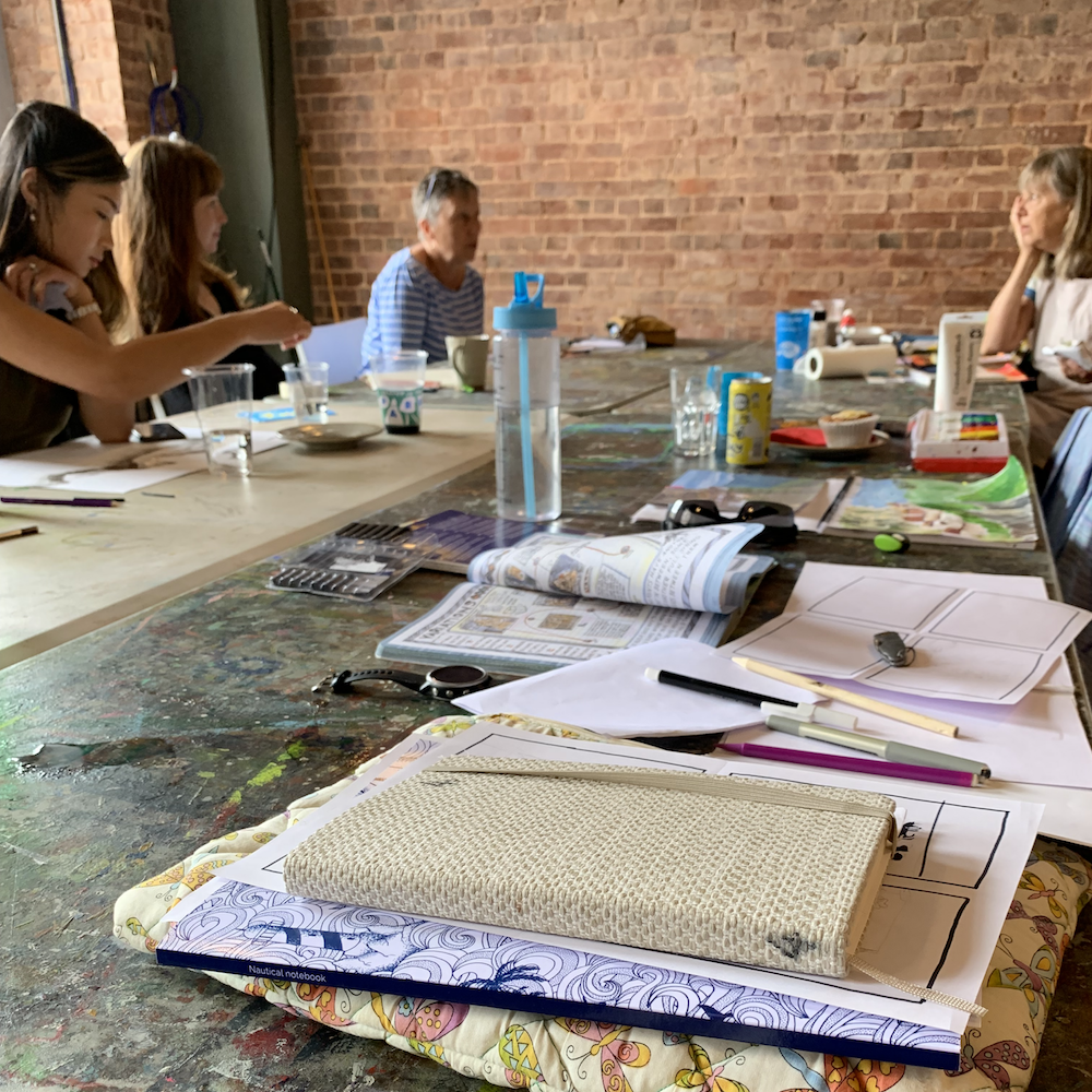 sketchbooks on a table with people sat around chatting