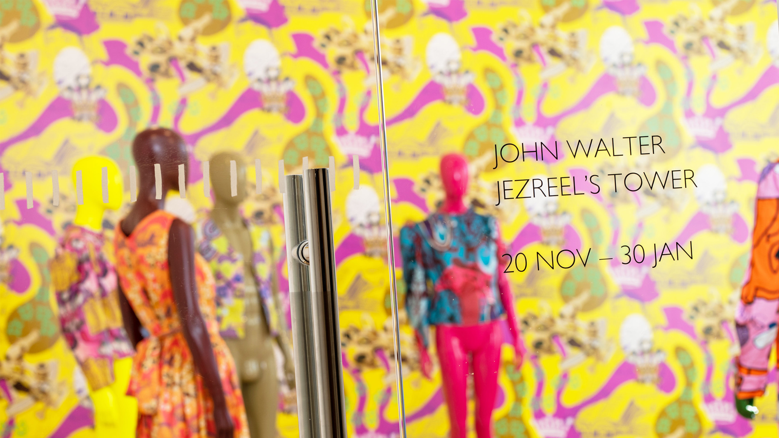 An installation shot of an exhibition which contains bright pink and yellow wallpaper, with mannequins dressed in colourful clothing