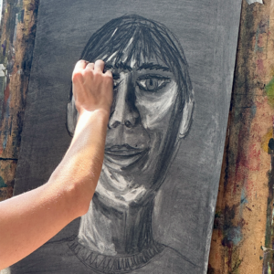 A hand sketching a face in charcoal and chalk