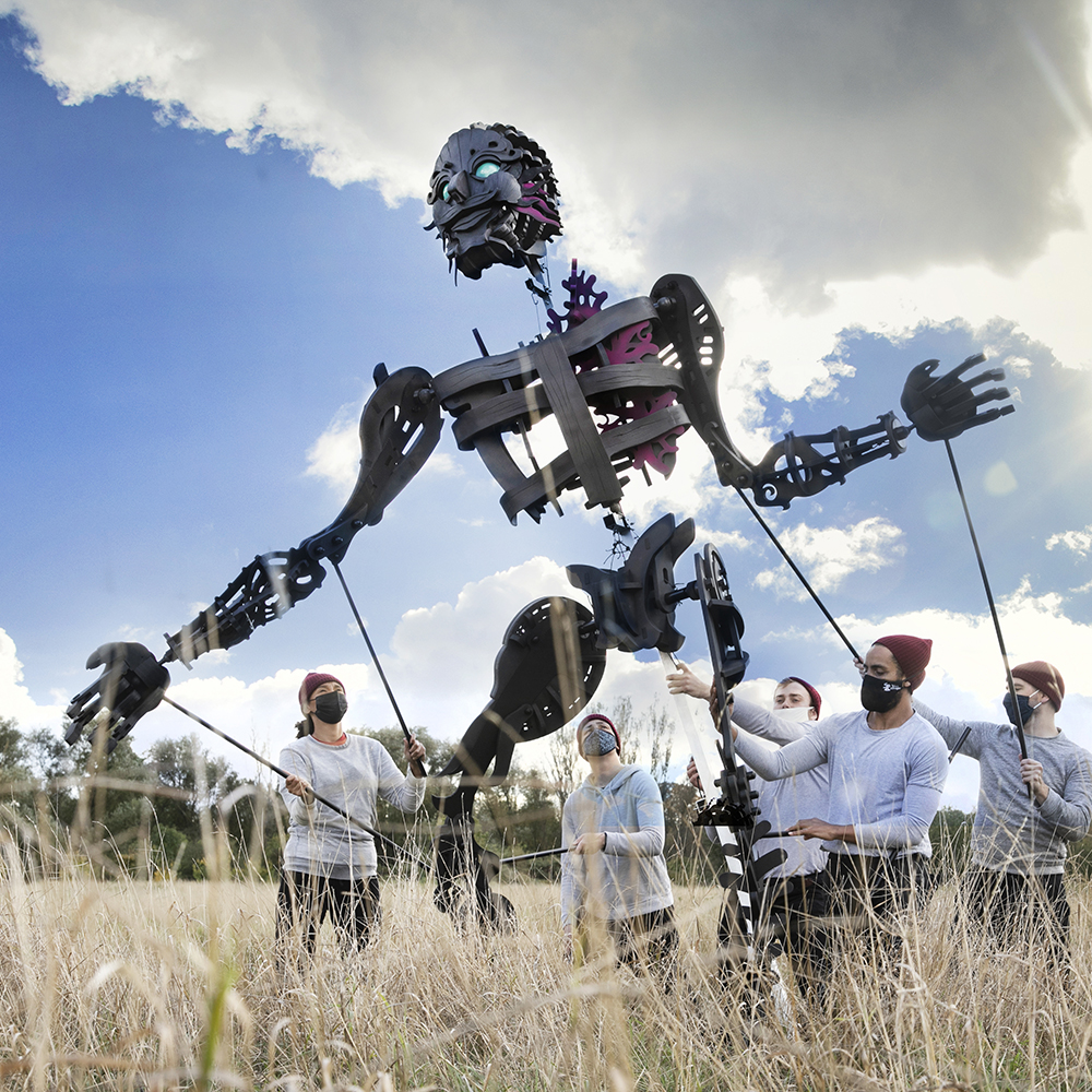 A large puppet in a field being moved by a team of people