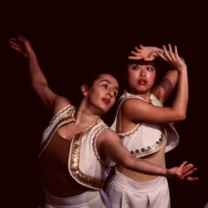Two dancers dressed in white with white makeup posing their arms