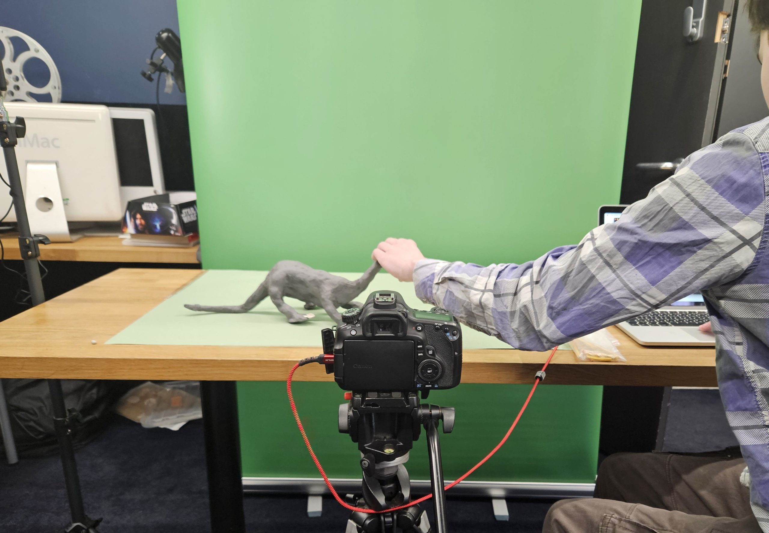 A young person moves a modelling clay dinosaur on a green screen while a camera records