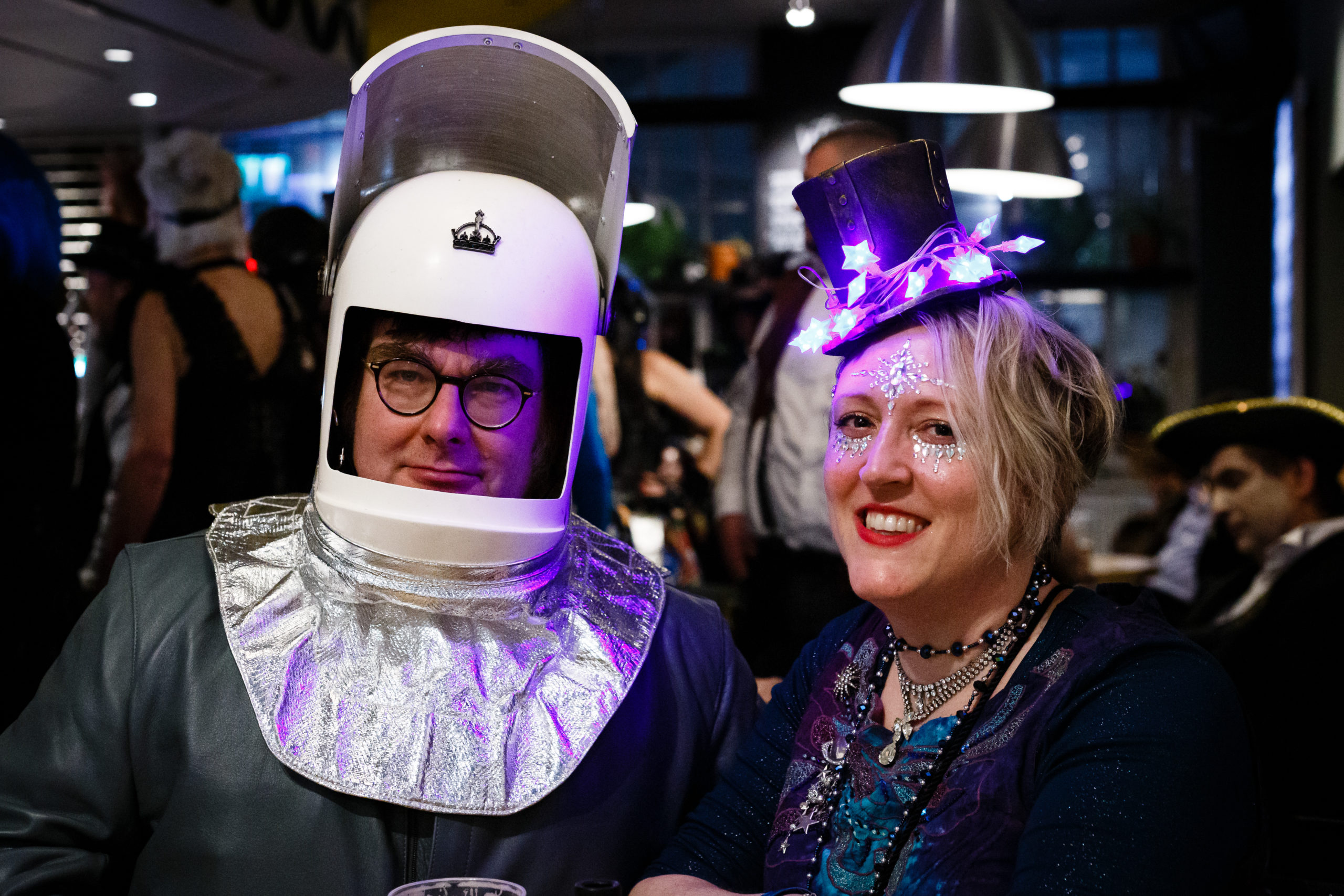 A man wearing a spaceman costume and a woman with jewels on her face and a light up top hat