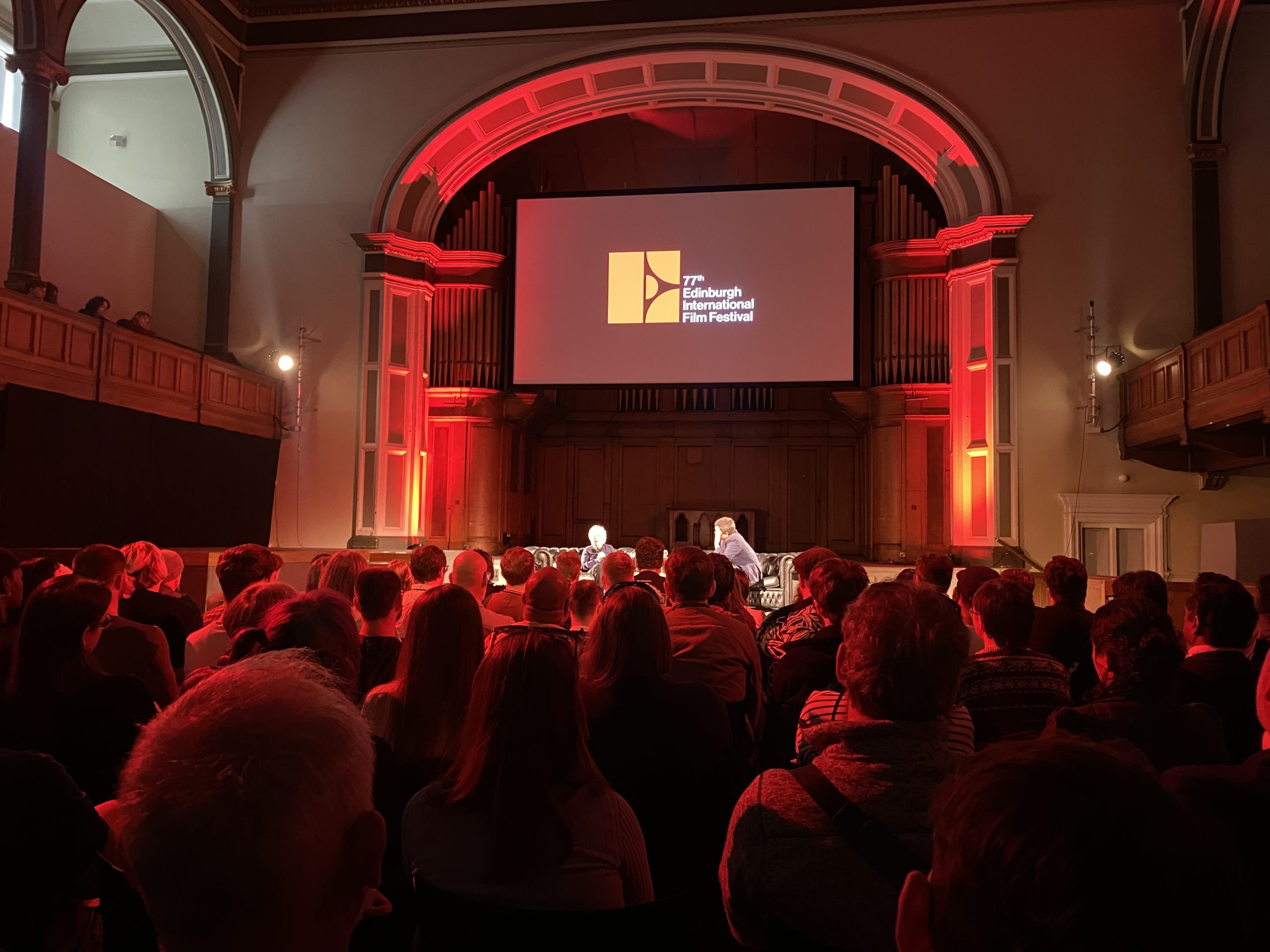 An audience sat in a hall with a screen saying '77th Edinburgh International Film Festival'