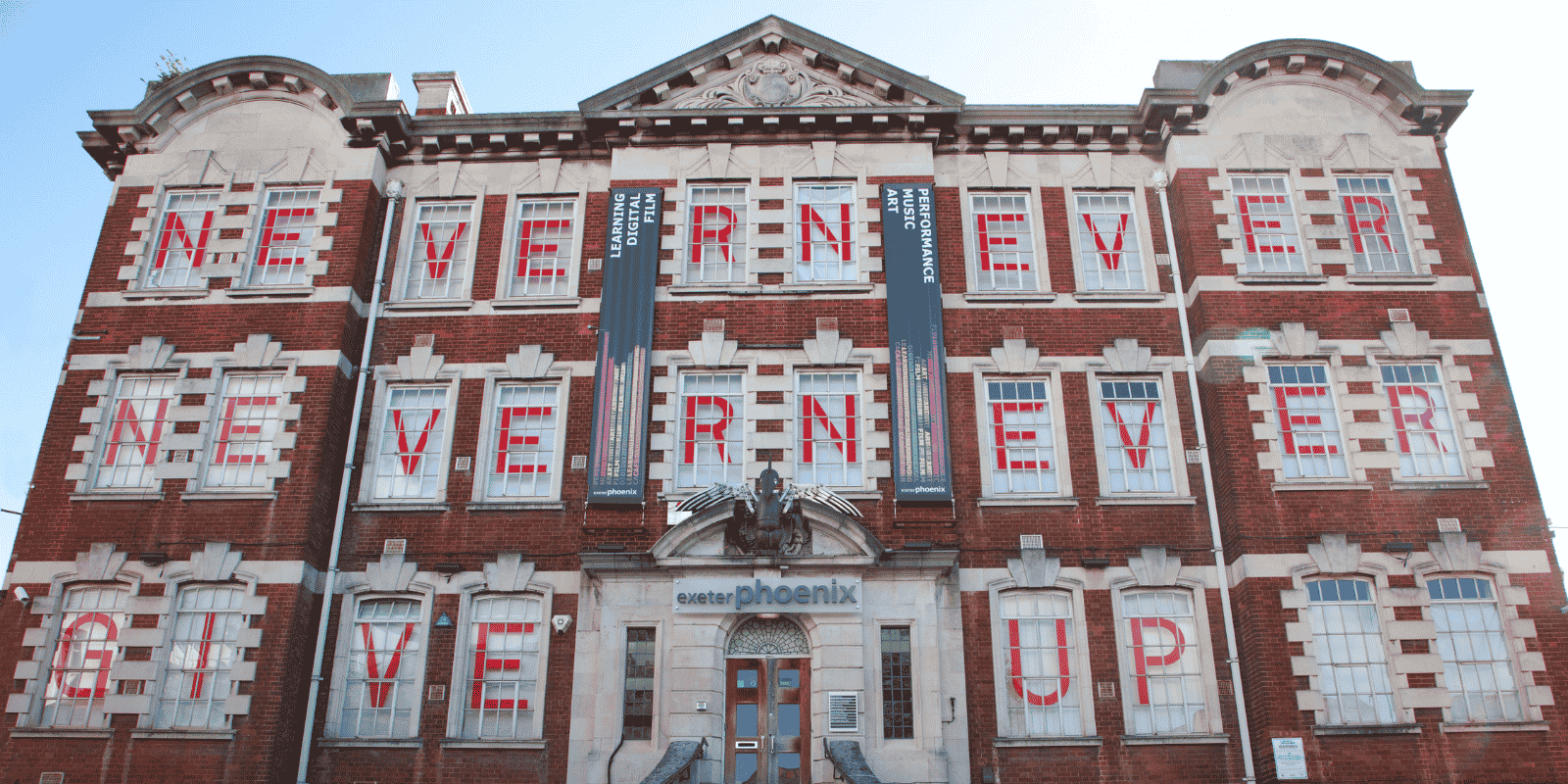 Photograph of the Exeter Phoenix building with red letters in the windows spelling out 'Never Never Never Give Up'