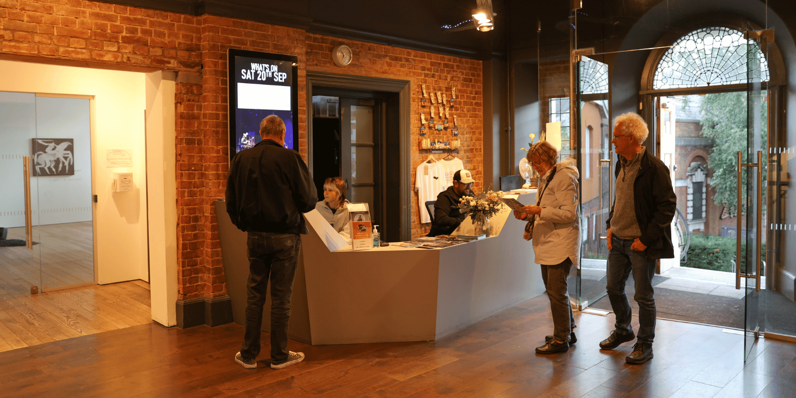 Opening Times Three people stand in the lobby of Exeter Phoenix being assisted by staff sat behind the Box Office.