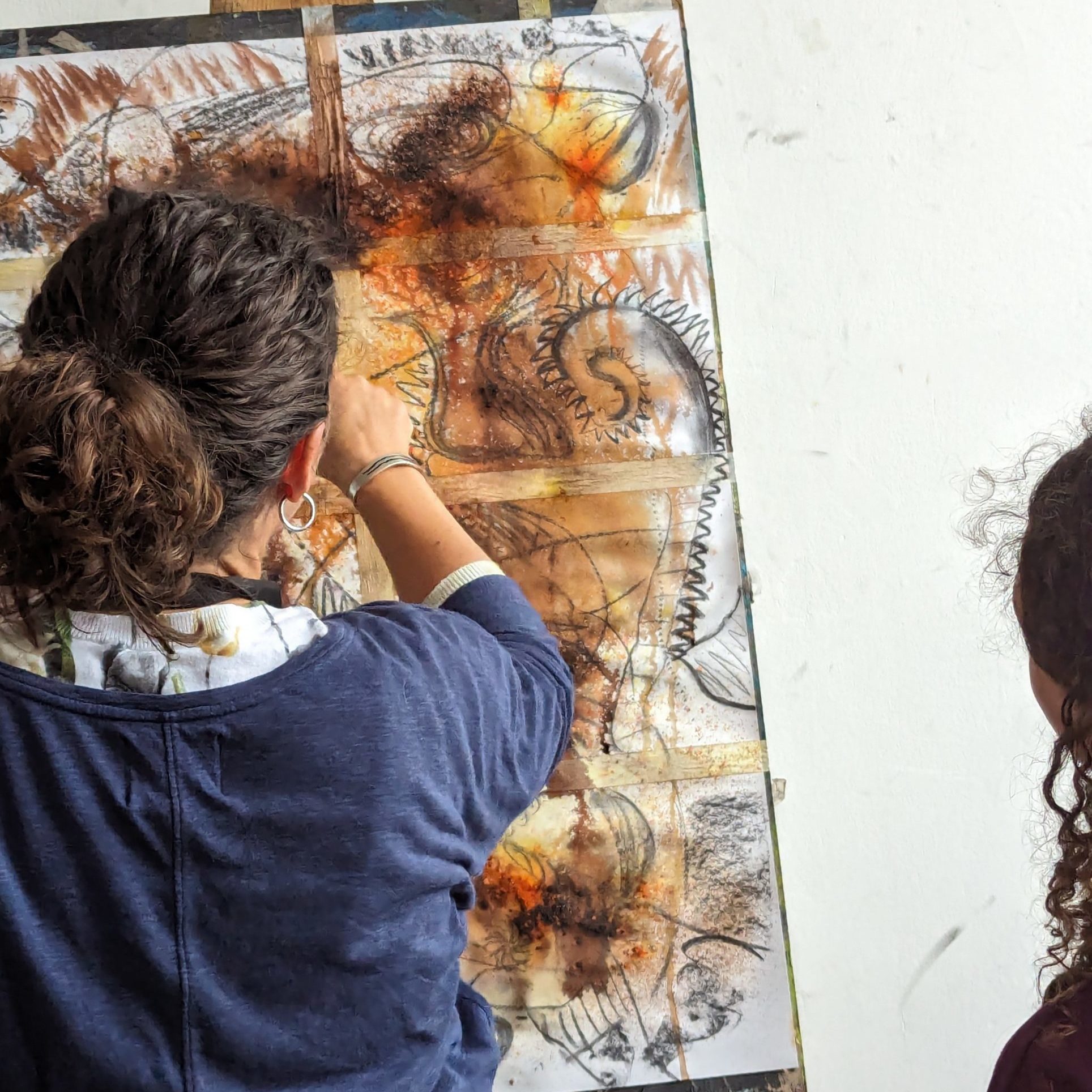 A lady drawing in charcoal over watercolour paints