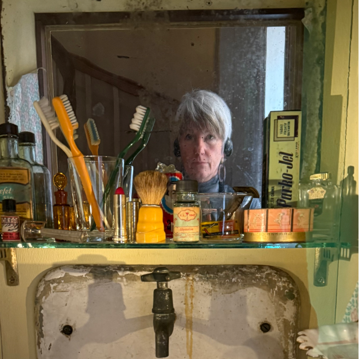 A woman looking in a mirror in a dirty bathroom.