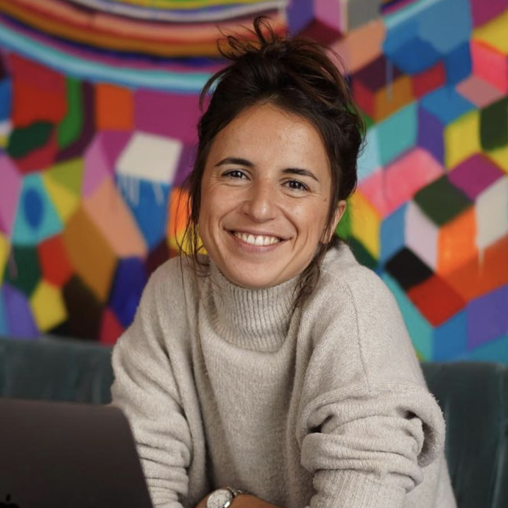 Woman staring into camera leaning onto table behind a computer.